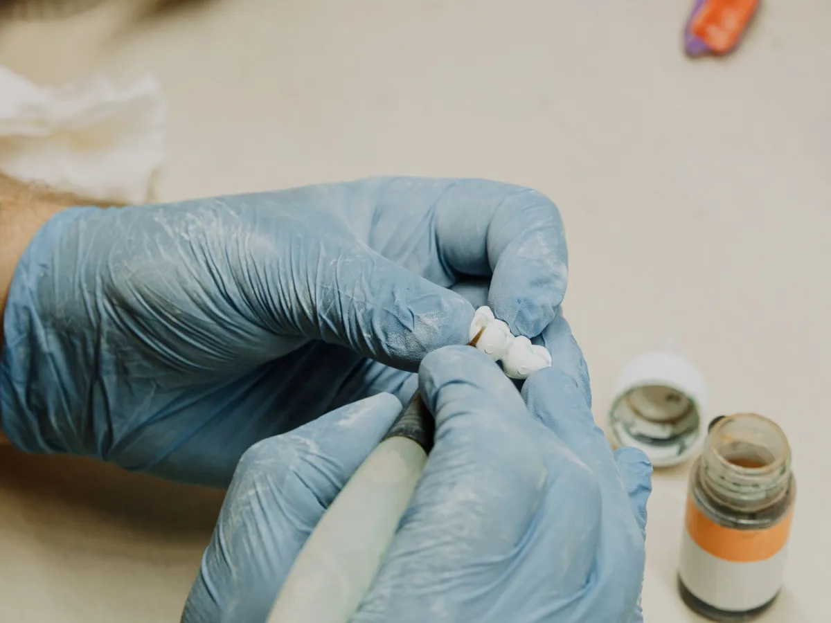 A lab technician hand-detailing a crown at the bench